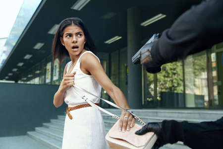 Robber want to steal handbag of scared girl. Cropped image of bandit wear black hoodie and...