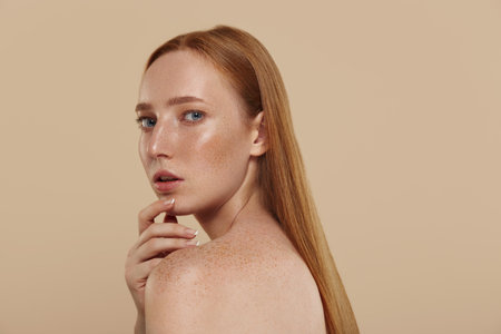 Redhead caucasian girl with naked shoulders. Cropped partial view of young beautiful red-haired woman with freckles. Natural female beauty. Isolated on beige background in studio. Copy spaceの写真素材