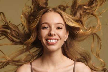 Smiling happy young white woman in underwear with long blonde curly hair standing over beige...