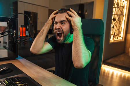 Angry devastated young man gamer wearing headphones lost a game on computer
