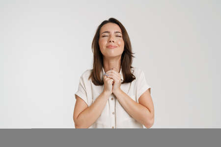 European woman posing with her eyes closed while making praying gesture isolated over white...