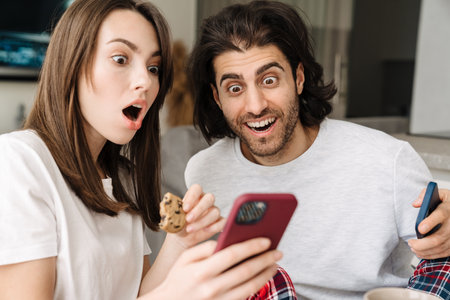 Young multiracial couple using cellphones while having breakfast together at homeの写真素材