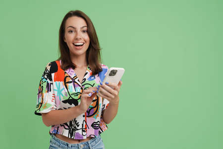 Young european woman smiling and using mobile phone isolated over green backgroundの写真素材