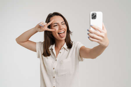 Young european woman taking selfie photo on mobile phone isolated over white backgroundの写真素材