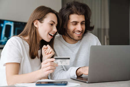 Young multiracial couple using credit card while working with laptop together at home