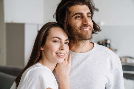Young multiracial couple smiling while hugging together at home