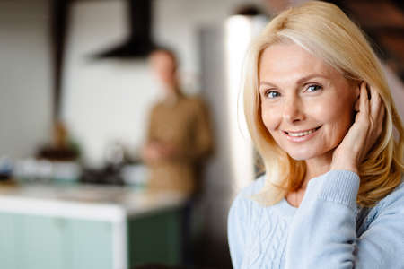 Smiling mid aged woman standing at the living room with her husband on a backgroundの写真素材