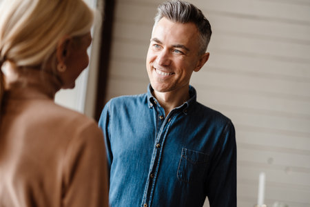Happy mid aged white couple standing in modern living room talkingの写真素材