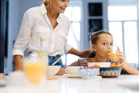 White mother and daughter smiling while having lunch in kitchen at homeの写真素材