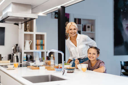 White mother and daughter smiling while having lunch in kitchen at homeの写真素材