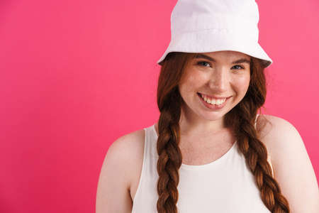 Young ginger woman with pigtails smiling and looking at camera isolated over pink background