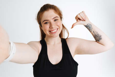 Ginger woman pointing finger at herself while taking selfie photo isolated over white background