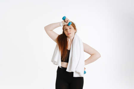 Tired exhausted young plus size fitness woman in sportswear standing over white backgroundの写真素材