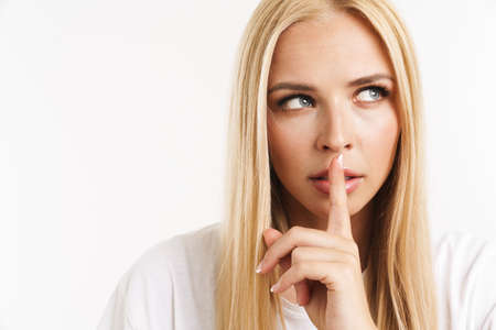 Young blonde woman in t-shirt showing silence gesture at camera isolated over white backgroundの写真素材