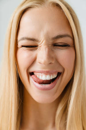 Young blonde woman smiling while licking her teeth isolated over white backgroundの写真素材