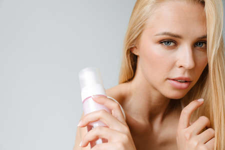 Young blonde woman looking at camera while showing washing foam isolated over white backgroundの写真素材