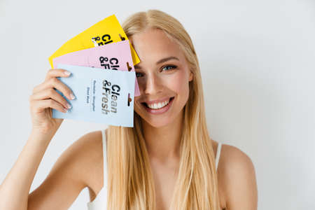 Young blonde woman smiling while showing cosmetic masks isolated over white backgroundの写真素材