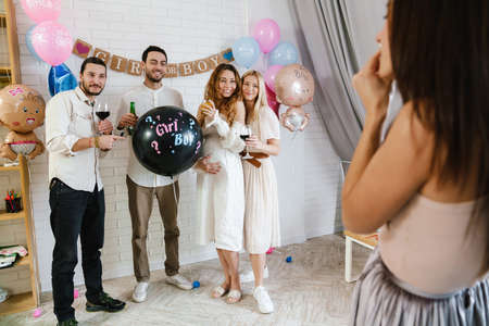 Group of happy friends at a gender reveal baby shower, holding balloon, taking a photo by a photographerの写真素材