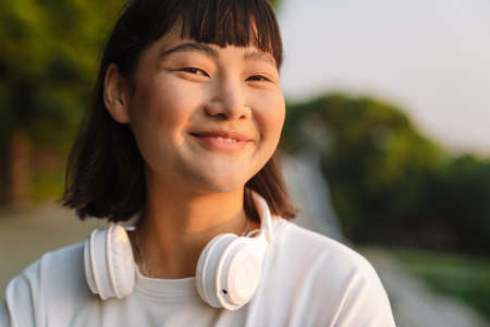 Smiling young asian woman walking in a green park enjoying listening to music with wireless headphones close upの写真素材