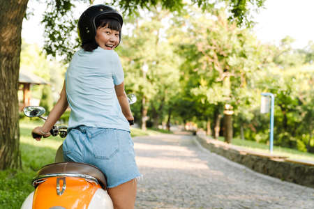 Close up of a smiling young asian woman wearing helmet riding motorbike at the parkの写真素材