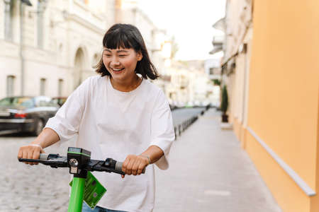 Smiling young asian woman driving electric scooter on a city streetの写真素材