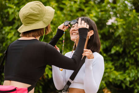 Multiracial two women wearing sunglasses while making fun together outdoors