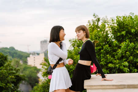Multiracial two women talking and smiling while walking together outdoorsの写真素材