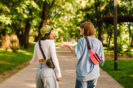 Multiracial two women talking and gesturing while walking together in green parkの写真素材