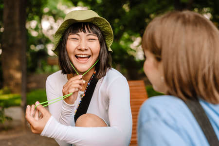 Multiracial two women talking and laughing while resting in green parkの写真素材