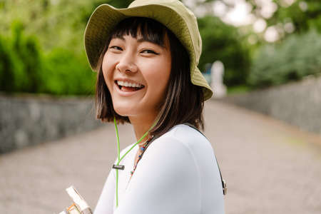 Young asian woman wearing hat smiling while walking at green parkの写真素材