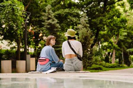 Multiracial two women talking and smiling while resting in green parkの写真素材