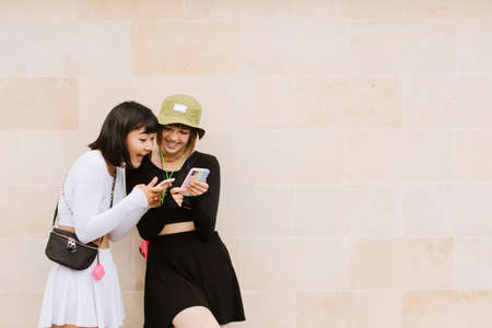 Multiracial two women using cellphones and smiling together outdoorsの写真素材
