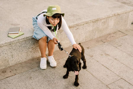 Young asian woman in hat smiling while walking with her dog outdoorsの写真素材