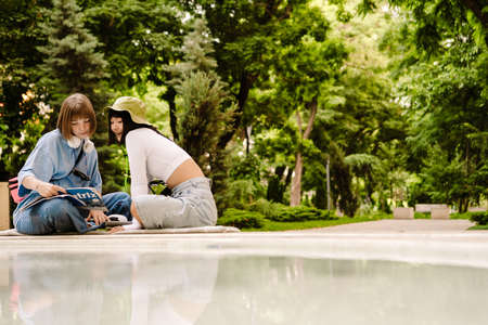 Multiracial two women talking and smiling while resting in green parkの写真素材