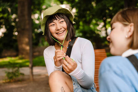 Multiracial two women talking and laughing while resting in green parkの写真素材