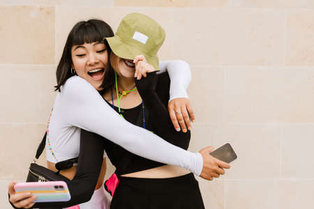 Multiracial two women making fun and taking selfie photo on cellphone outdoors