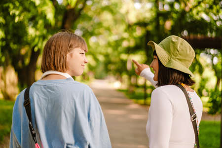 Multiracial two women talking and gesturing while walking together in green parkの写真素材