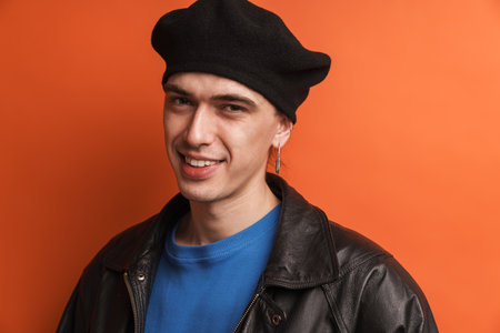 Young smiling fashionable white man wearing leather jacket and beret standing posing over red backgroundの写真素材