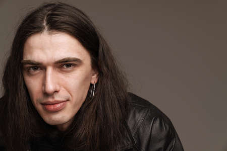 Young smiling fashionable white man wearing leather jacket standing posing over gray background looking at camera close upの写真素材