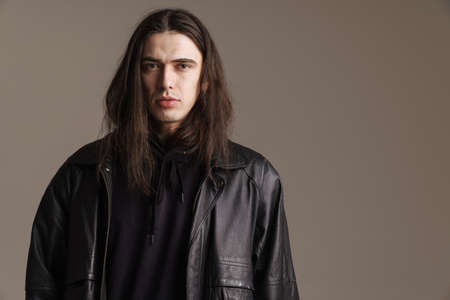 Young fashionable white man wearing leather jacket standing posing looking at camera over gray backgroundの写真素材