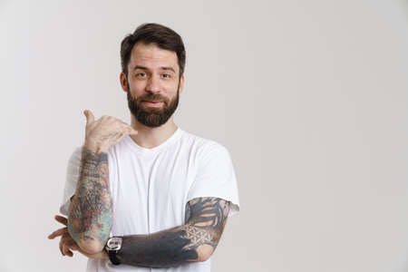 Bearded white man with tattoo smiling and gesturing at camera isolated over white backgroundの写真素材