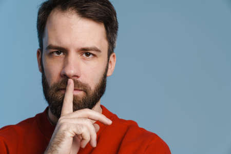 Brunette white man with beard smiling and showing silence gesture isolated over blue backgroundの写真素材