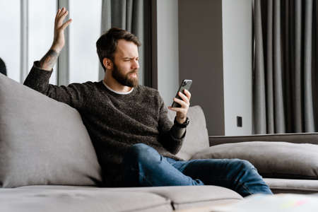 Bearded european man using mobile phone while sitting on sofa at homeの写真素材