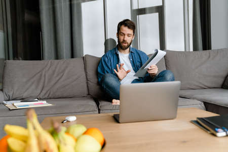 Bearded european man working with laptop while sitting on sofa at home