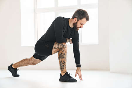 Confident mid aged white sportsman exercising in a bright room doing lunges