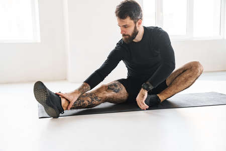 Bearded sportsman with tattoo doing exercise while working out indoors