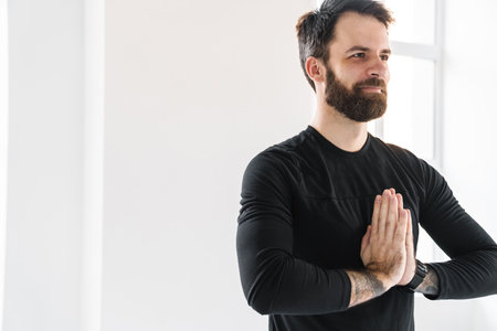 Smiling mid aged white sportsman exercising in a bright room standing with palms together meditatingの写真素材