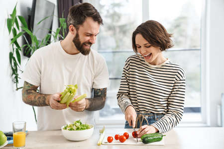 Young happy white couple cooking salad together in the kitchen at homeの写真素材