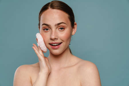 Smiling young healthy woman applying makeup with powder puff over blue backgroundの写真素材