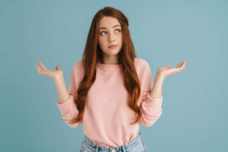 Young ginger woman looking upward while holding copyspace isolated over blue background